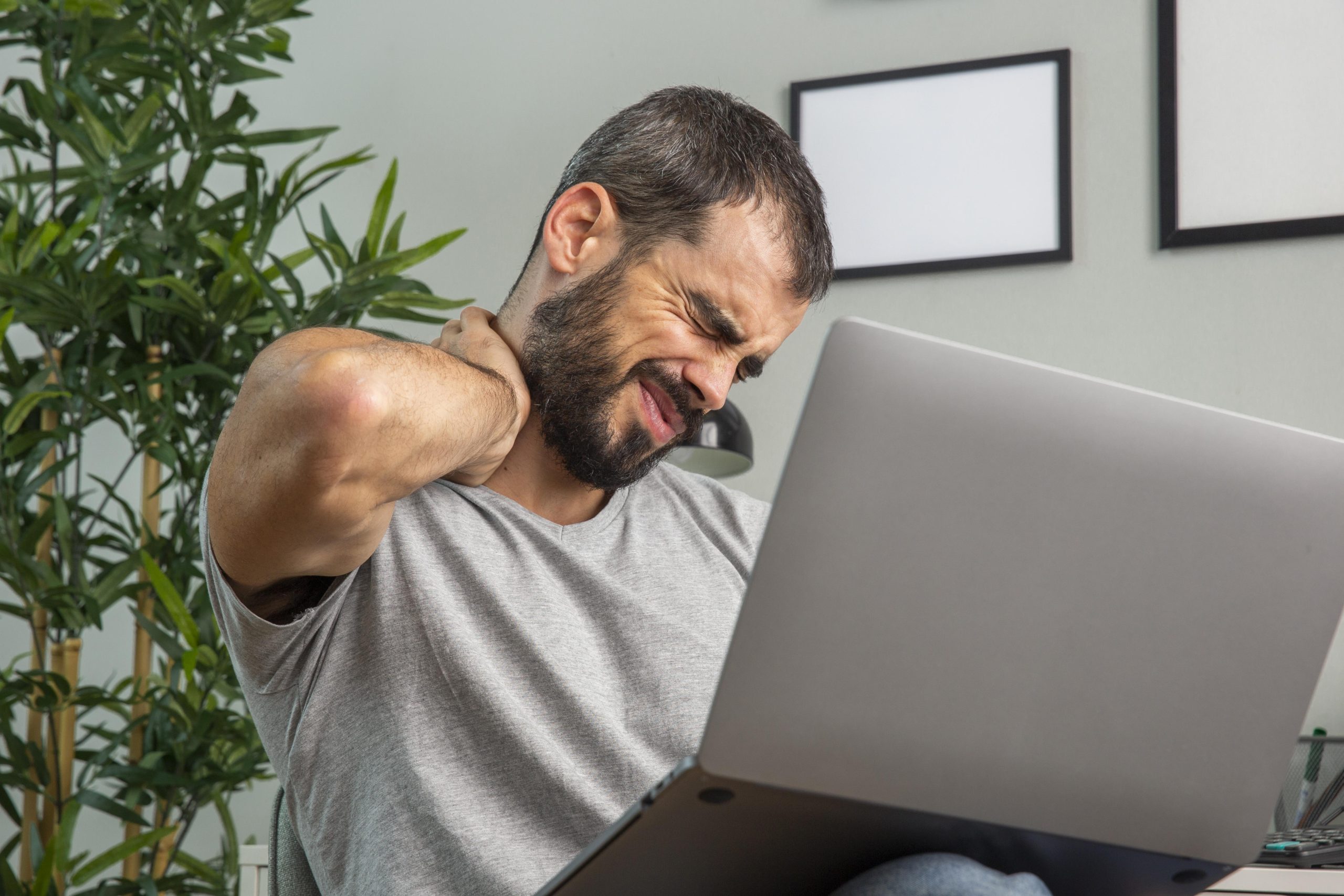 man experiencing neck pain while working from home laptop